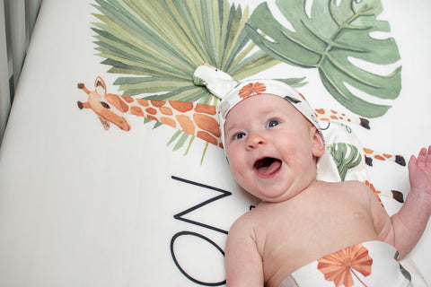 Baby in a giraffe theme blanket and sheet, wearing a giraffe hat